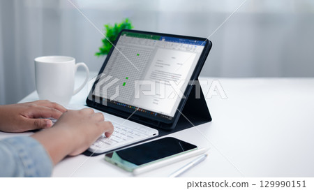Close up of hands typing on wireless keyboard connected to tablet showing spreadsheet and document, concept of remote work, data analysis, project management, and business productivity. Close up of hands typing on wireless keyboard connected to tablet showing spreadsheet and document, concept of remote work, data analysis, project management, and business productivity. 129990151
