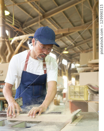 Senior craftsman cutting wood with a circular saw 129990315