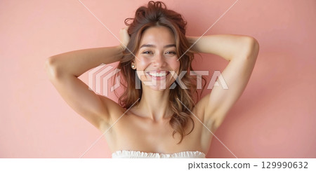 Smiling young woman posing playfully against pink background in casual summer outfit 129990632