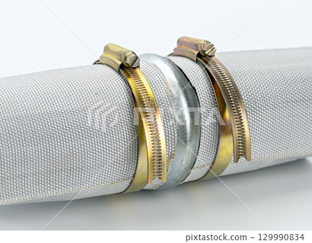 Two metal pipe connector with brass strap industrial hose clamp silver and gold color close up mechanical equipment plumbing fitting isolated on white background durable secure connection 129990834