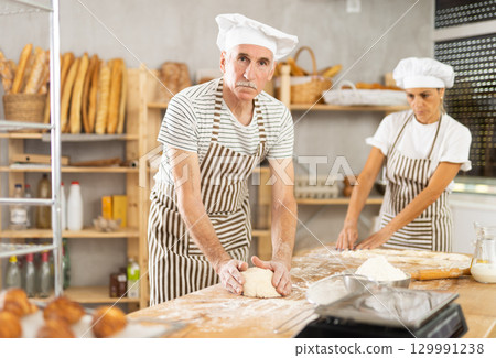 Elderly man and woman kneading and braiding dough 129991238