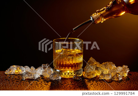 Whiskey pours from bottle to glass. Whiskey pours from bottle to glass. 129991784