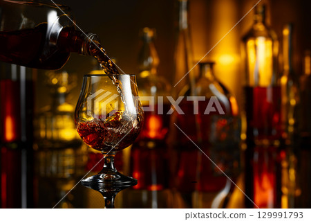 Pouring brandy from a bottle into a glass. 129991793