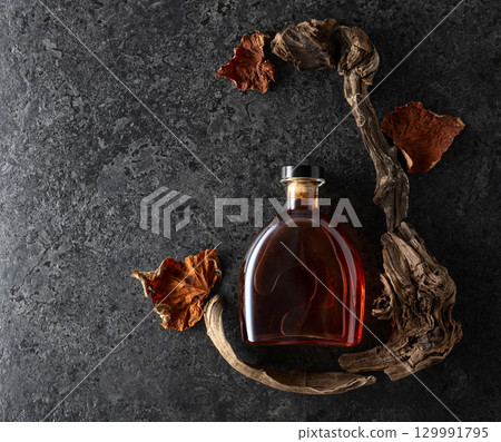 Bottle of brandy and old snags with dried up vine leaves. Bottle of brandy and old snags with dried up vine leaves. 129991795
