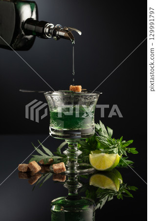 Absinthe is poured from an vintage bottle into a glass. Absinthe is poured from an vintage bottle into a glass. 129991797