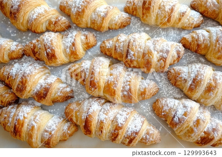 Top-down view of freshly baked croissants on parchment paper, sprinkled with powdered sugar. 129993643
