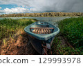 One boat is moored on the bank of a calm river, with a blue cloudy sky in the background 129993978