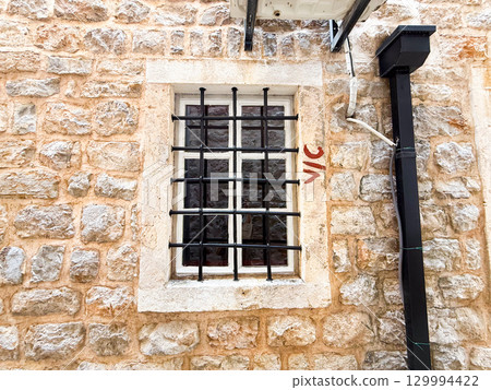 Small barred window in a rustic stone facade. Architecture, security, tradition and history in an old European street. 129994422