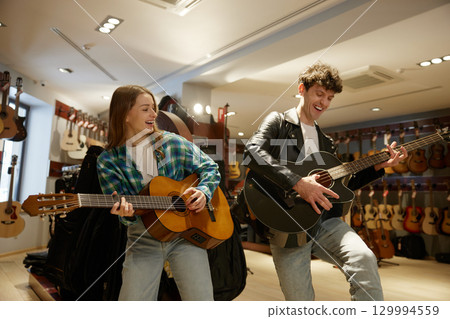 In a music store, a man and a woman are playing their guitars skillfully In a music store, a man and a woman are playing their guitars skillfully 129994559