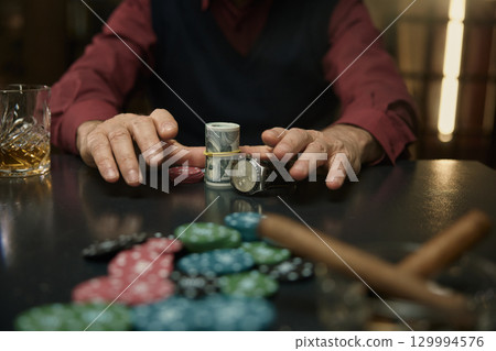 Thrilling moment at poker table with chips, stylish watch, and drink in dimly lit setting 129994576