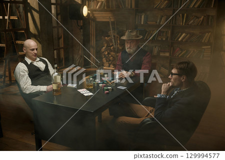 Three gentlemen playing poker game in a vintage old library 129994577