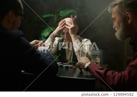 An intense poker game featuring men company unfolds in a smoke-filled room 129994582