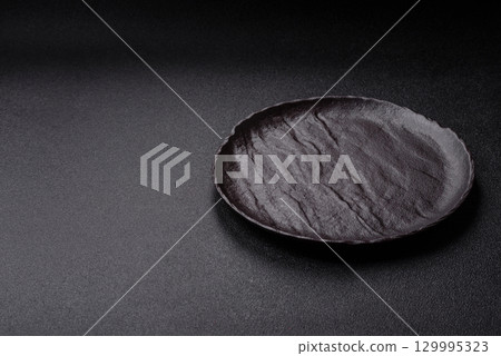 Empty round black plate for food, risotto or pasta. Empty plate on dark background Empty round black plate for food, risotto or pasta. Empty plate on dark background 129995323