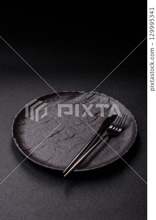 Empty round black plate for food, risotto or pasta. Empty plate on dark background Empty round black plate for food, risotto or pasta. Empty plate on dark background 129995341