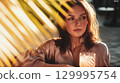 Beautiful woman enjoying a cocktail in the golden hour sunlight, relaxed. A young woman gazes thoughtfully, illuminated by sunlight filtering through palm fronds This is AI-generated item 129995754