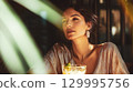 Elegant woman enjoying a cocktail in a bar, bathed in warm sunlight. A beautiful woman enjoys a refreshing cocktail, illuminated by sunlight, exuding elegance This is AI-generated item 129995756