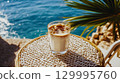 Iced coffee with a view of the ocean is the perfect refreshment for a hot day. A refreshing iced coffee sits on a woven table with the ocean and a palm frond in background This is AI-generated item 129995760