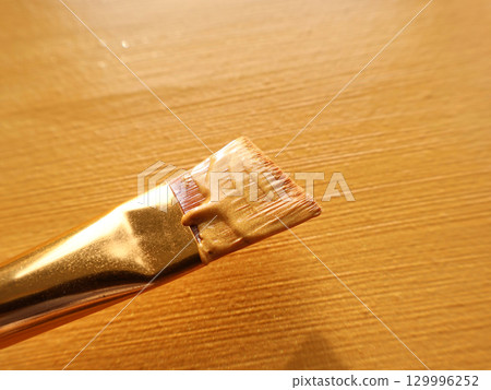 Close-Up of Paintbrush With Gold Tone Handle on Wooden Surface 129996252