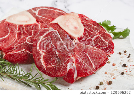 knuckle on the bone, raw meat for ossobuco, on a wooden chopping board, with a sprig of rosemary, and spices, top view, no people, 129996292