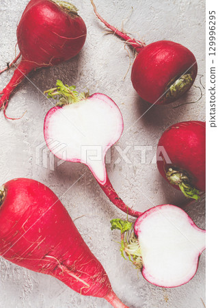 Fresh red radishes cut in half with green tops on a neutral background in a kitchen setting 129996295