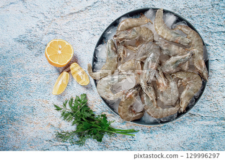 Fresh raw shrimp spread on ice with lemon and cilantro slices on a marble surface, ready to cook, no people 129996297
