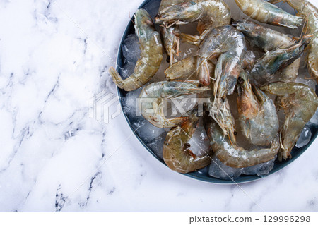 Fresh raw shrimp spread on ice with lemon and cilantro slices on a marble surface, ready to cook, no people 129996298