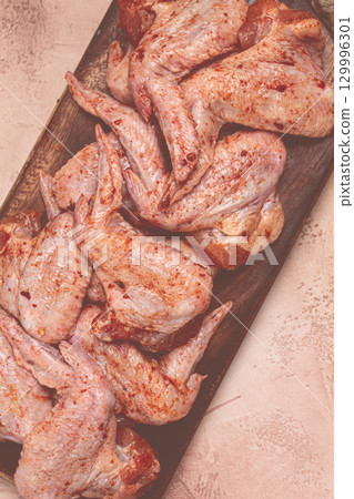 Chicken wings, marinated and laid out on a wooden platter, ready for cooking, grilling or baking, in a home kitchen, there are no people 129996301