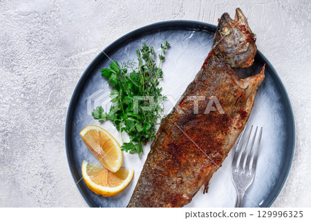 fried rainbow trout, with herbs and citrus fruits, on a plate, top view, 129996325