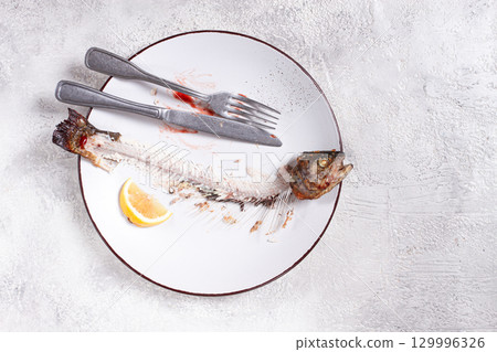 The remains of fish on a plate with a fork and knife, the skeleton of a rainbow trout, after lunch, top view, no people, 129996326