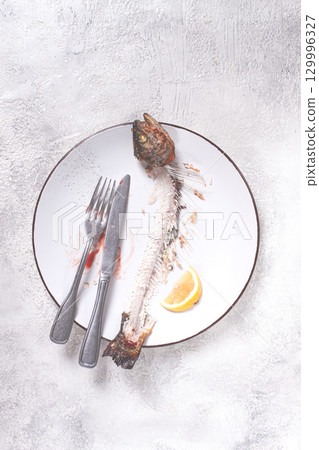 The remains of fish on a plate with a fork and knife, the skeleton of a rainbow trout, after lunch, top view, no people, 129996327