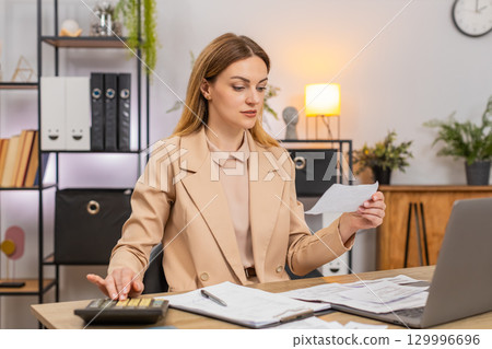 Businesswoman sorts receipts uses calculator balances budget signs final contract with pleased smile Businesswoman sorts receipts uses calculator balances budget signs final contract with pleased smile 129996696