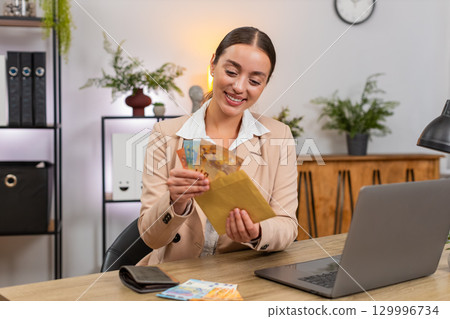 Young businesswoman counts euro cash from wallet plans budget and puts part into reserve envelope 129996734
