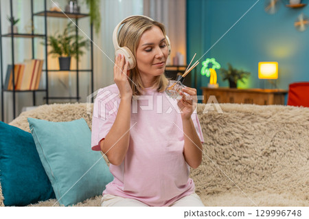 Pregnant woman inhaling aroma from diffuser with headphones relaxing music hugging belly calm deep 129996748