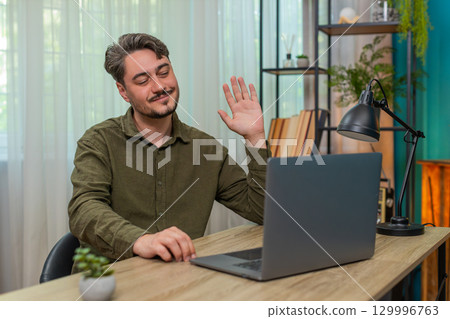 Middle-aged man smiling gesturing video call on laptop talking happily communicating online at table Middle-aged man smiling gesturing video call on laptop talking happily communicating online at table 129996763