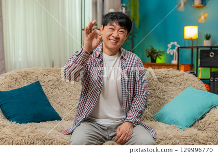 Asian cheerful man smiling at camera giving OK gesture positive assurance confirming everything fine Asian cheerful man smiling at camera giving OK gesture positive assurance confirming everything fine 129996770