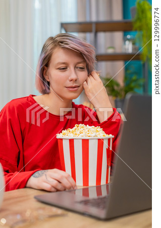 Woman watching funny movie on laptop eating popcorn, laughing, relaxed joyful leisure entertainment 129996774