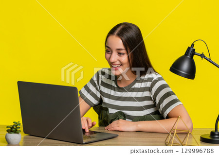Woman at table laughing while scrolling laptop screen watching funny entertaining online content Woman at table laughing while scrolling laptop screen watching funny entertaining online content 129996788