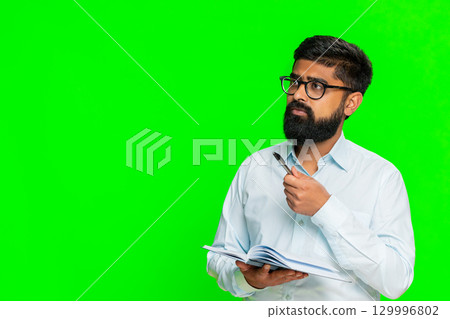 Indian man writing in notebook focused face planning daily tasks to-do list concentration gesture 129996802