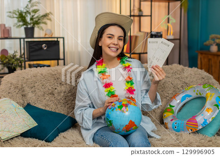 Young woman on sofa with swim ring holding globe and plane tickets planning exciting future trip 129996905