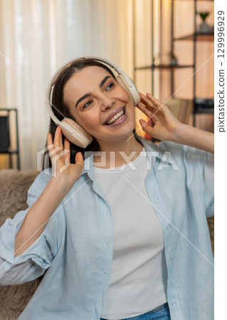 Young woman on sofa wearing headphones dancing moving head rhythmically enjoying music happily 129996929