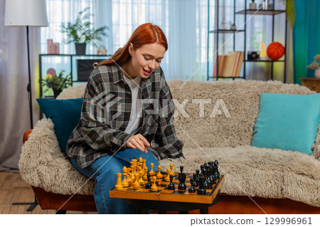 Woman on sofa playing chess against herself smiling having fun with playful split personality mood Woman on sofa playing chess against herself smiling having fun with playful split personality mood 129996961