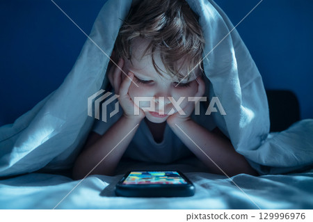 Child Watching Smartphone Under Blanket at Night Child Watching Smartphone Under Blanket at Night 129996976