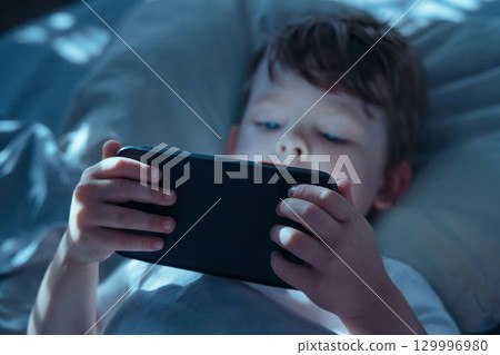 Child Watching Smartphone Screen in Bed at Night 129996980