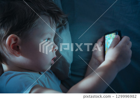 Child Watching Smartphone Screen in Bed at Night Child Watching Smartphone Screen in Bed at Night 129996982