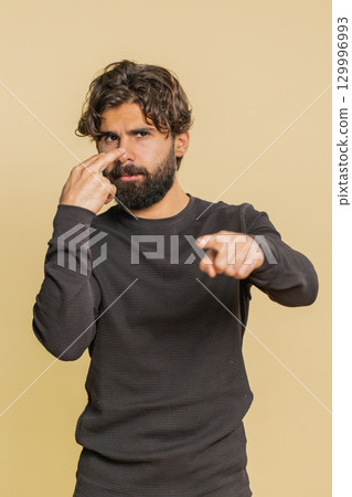 Confident young Indian man guy showing I am watching you gesture against beige studio background Confident young Indian man guy showing I am watching you gesture against beige studio background 129996993
