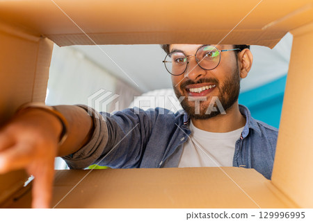 Happy Indian man shopper unpacking cardboard box delivery parcel online shopping purchase at home 129996995