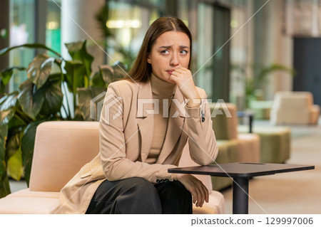 Depressed desperate young businesswoman feeling worried about financial problems in office lobby Depressed desperate young businesswoman feeling worried about financial problems in office lobby 129997006