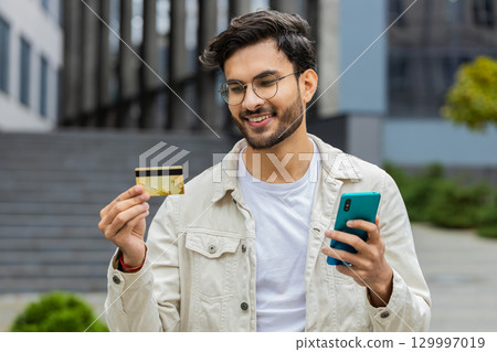 Indian man using credit bank card smartphone while transferring money, purchases online shopping Indian man using credit bank card smartphone while transferring money, purchases online shopping 129997019