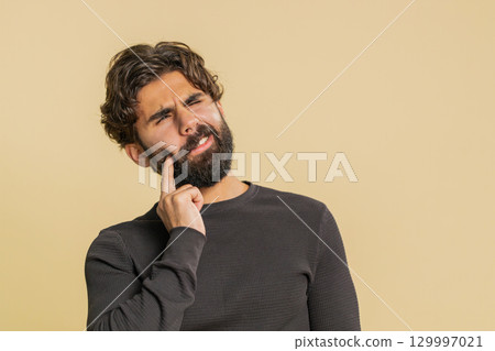 Young Indian bearded man touching sore cheek suffering from toothache cavities on beige background 129997021