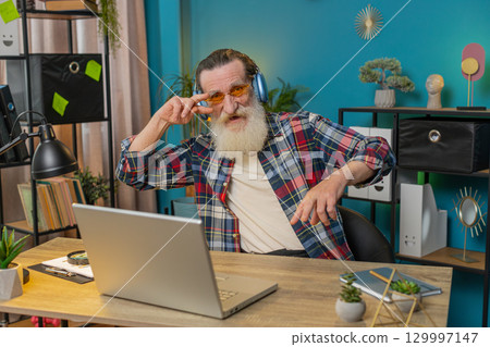Happy senior man listening music through wireless headphones relaxing taking a break with laptop Happy senior man listening music through wireless headphones relaxing taking a break with laptop 129997147